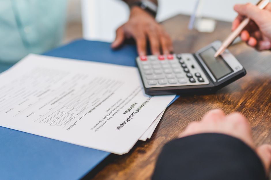 Hands using a calculator with real estate documents on a desk, indicating a financial transaction or meeting.