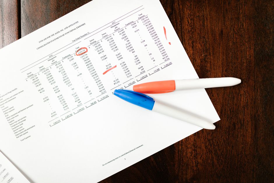 Top view of financial document with red marks and pens on wooden table surface.